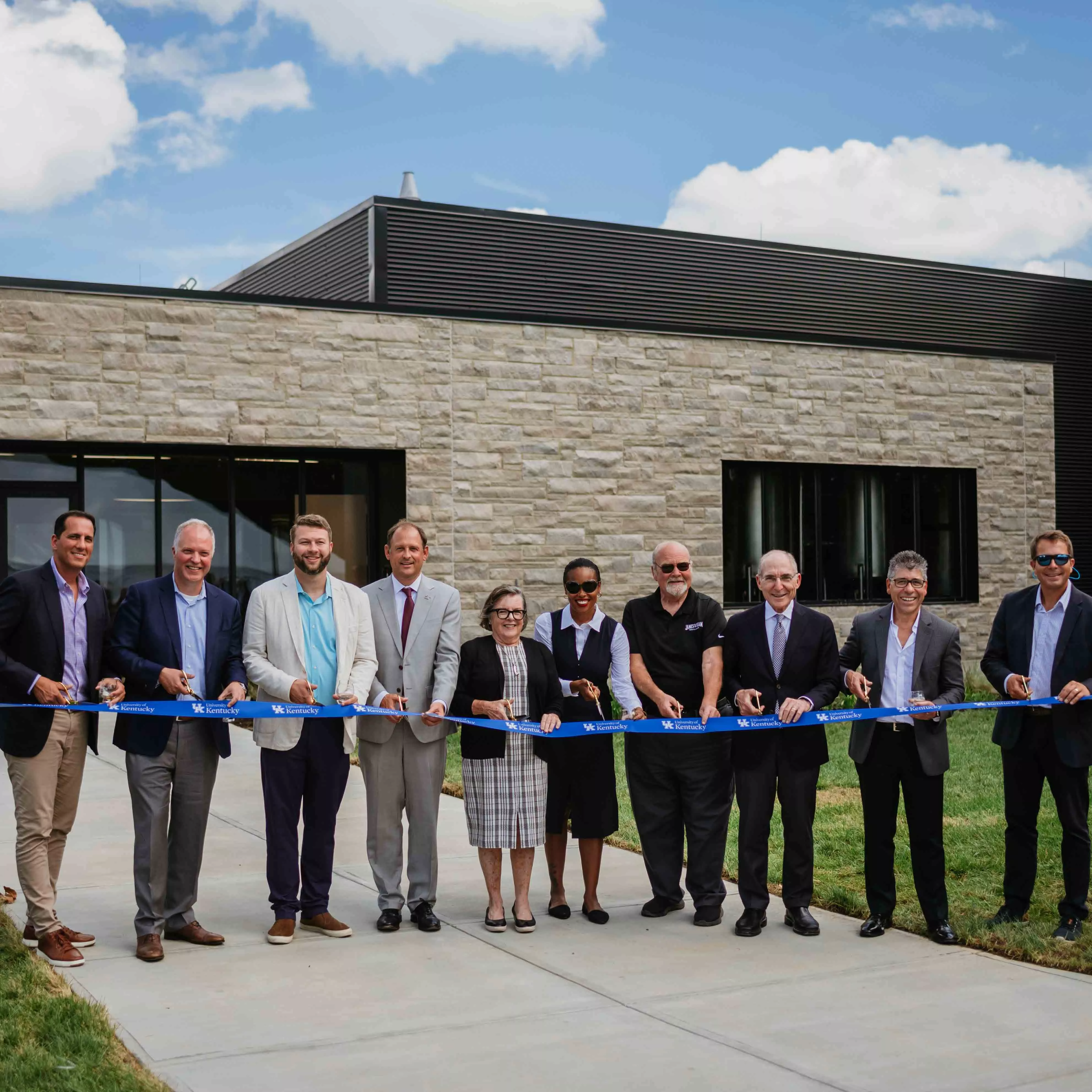 A line of Jim Beam employees stand in front a blue ribbon for the ceremonial opening of a new Beam centre.
