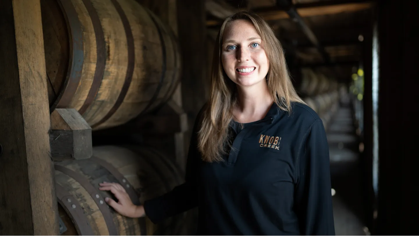 A Knob Creek Bourbon distillery worker stands in a cellar, beside barrels of Bourbon.