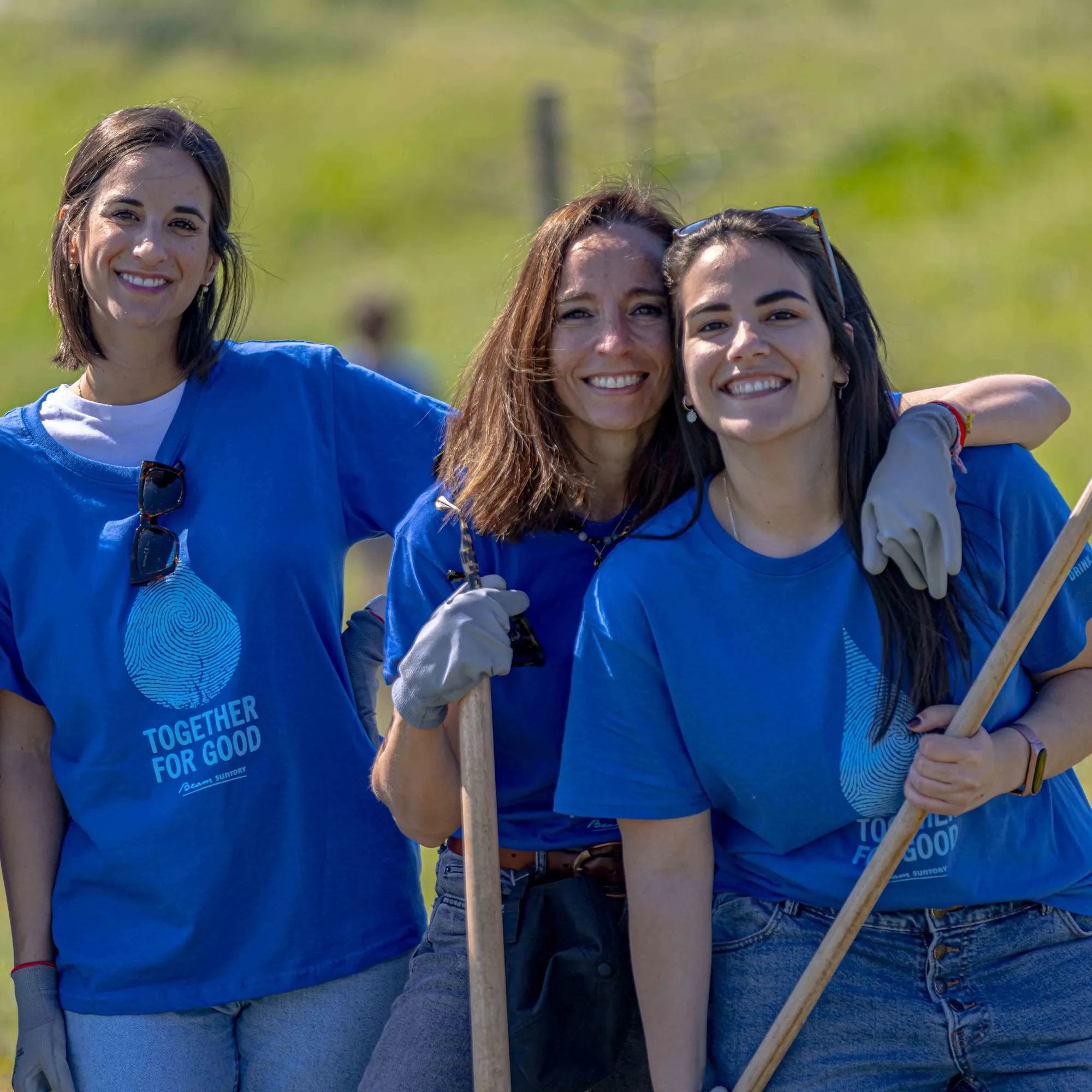 Three sustainability project workers hold agricultural tools as they rest