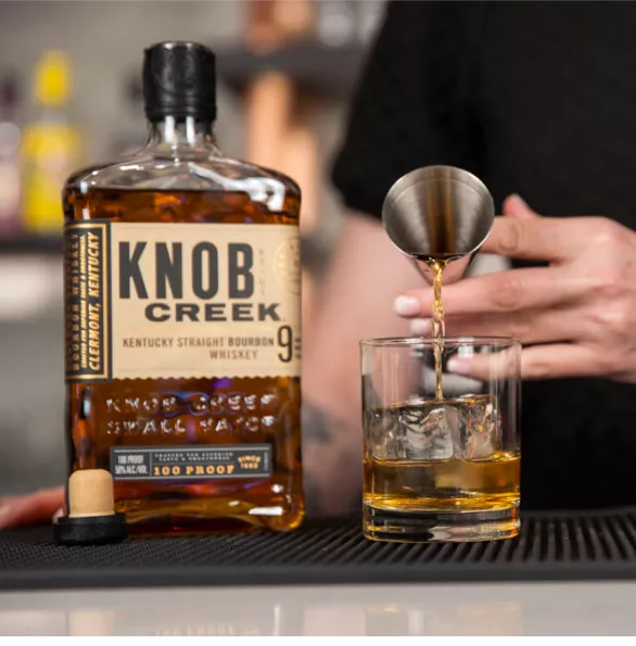 A skilled hand pours a mesaure of Knob Creek bourbon whisky into a glass filled with ice.